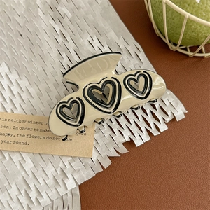 Detail of cream acetate hair claw clip with black heart cutouts on a vintage background