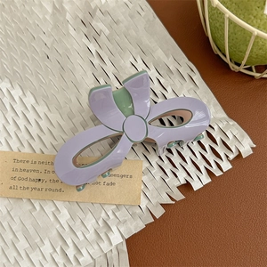 Detail view of purple and green bow-shaped acetate hair claw clip on soft paper