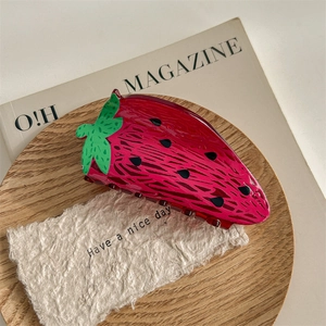 Détail d'une pince à cheveux en forme de fraise rouge brillante avec des feuilles vertes