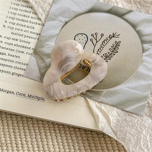 Detailed macro view of heart-shaped cream marble acetate claw clip with gold metal teeth