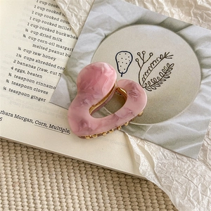 Detailed view of heart-shaped pink marble acetate hair claw clip with golden metal teeth