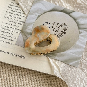 Detail of heart-shaped acetate hair claw with marble amber pattern and gold metal teeth