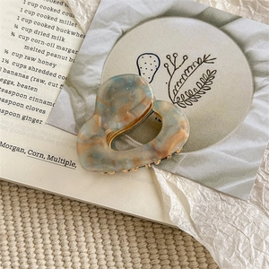 Close-up of heart-shaped marble acetate hair claw clip with golden metal teeth
