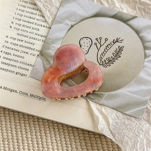 Detailed macro view of heart-shaped marbled purple hair claw with gold metal teeth
