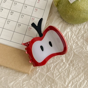 Macro shot of cute red apple slice hair claw clip with black seeds on beige fabric