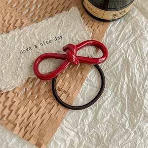Macro detail of glossy dark red acetate bow hair tie with black elastic band on paper