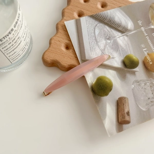 Detailed close-up of a pink acetate hair clip with golden metal edges on a tray