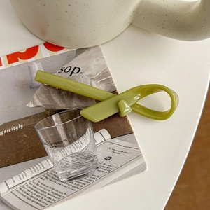Détail d'une pince à cheveux verte en acétate avec un design noué mat sur un magazine