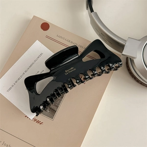 Macro detail of glossy black hair claw clip with gold engraving and hollow geometric design