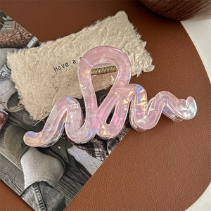 Détail d'une pince à cheveux rose nacré ondulée avec ressort en métal doré sur cuir