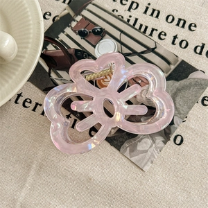 Detail of pink pearlescent flower hair claw clip with golden metal spring on fabric