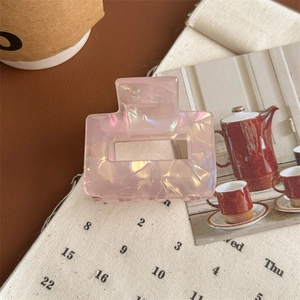 Detailed close-up of a square iridescent pink marble acetate hair claw clip on a retro desk