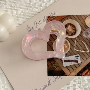 Détail d'une pince à cheveux en forme de cœur rose irisé avec ressort en métal doré