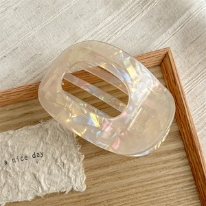 Detail of a beige iridescent hair claw clip with cutout design on a wooden tray