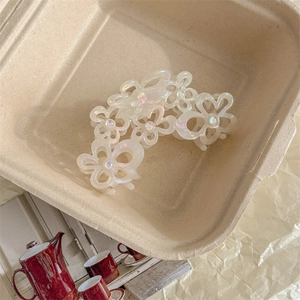 Dettaglio molletta a fiore perlato con petali traforati e strass di perle su carta color crema