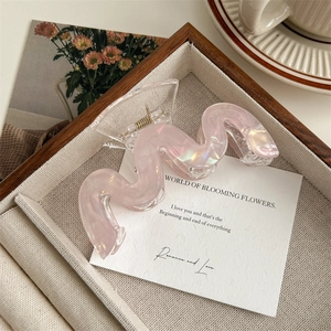 Détail d'une pince à cheveux ondulée rose irisé sur carte blanche et plateau en bois