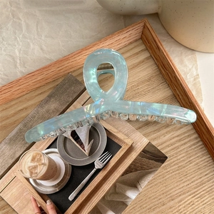 Detail of large iridescent light blue acetate shark hair claw on a wooden tray