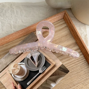 Detail of a large iridescent pink hair claw clip on a wooden tray with lifestyle coffee setting