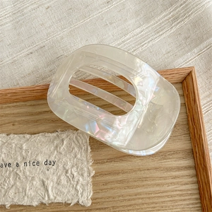 Close-up of iridescent semi-circular hair claw clip on wooden tray with linen background