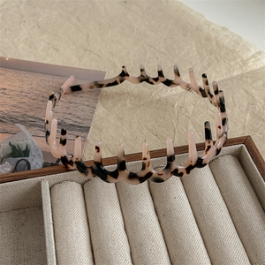 Detail of pink tortoiseshell headband with teeth design on beige jewelry box display