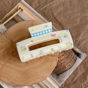 Detail of floral hair claw clip with blue plaid pattern and pink bow on wood base