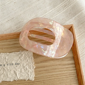 Detail view of large oval iridescent pink acetate hair claw clip on wooden tray