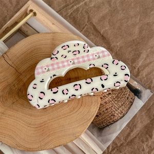 Detail of cream floral checkered hair claw clip with leopard print on a wooden tray