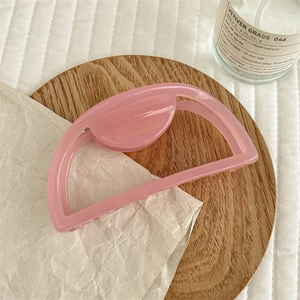 Detailed close-up of a pink semi-circle hair claw clip with golden handmade logo text