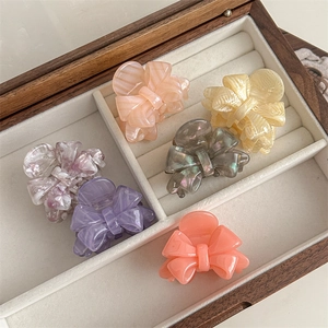 Elegant cellulose acetate bow hair claws in six marble colors displayed in a jewelry box