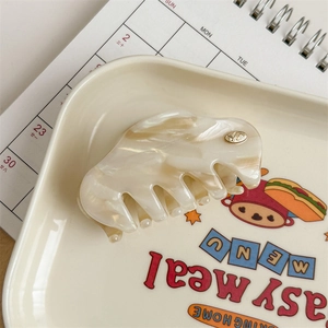 Macro detail of marble pattern hair claw with YD metal logo on cream tray