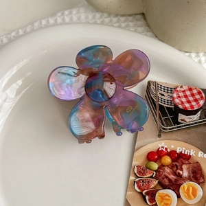 Detail of a floral acetate hair claw with iridescent gradient colors on a white plate