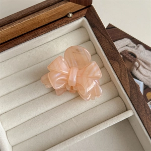 Macro shot of peach pink bow hair claw clip with marble texture on white velvet