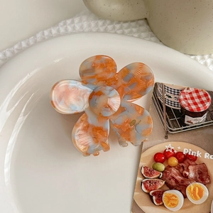 Detail of flower-shaped marble pattern acetate hair claw clip on a white ceramic plate
