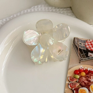 Macro shot of white acetate flower hair claw with pearl-like luster in ceramic tray
