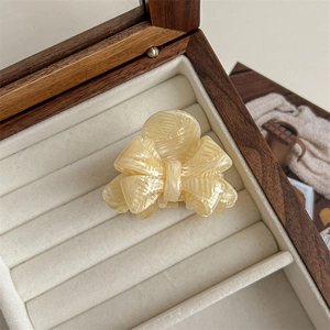 Detail view of a cream marble acetate bow hair claw clip in a velvet jewelry box