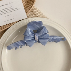 Blue marble acetate hair claw clip with bow detail and gold tag on ceramic tray