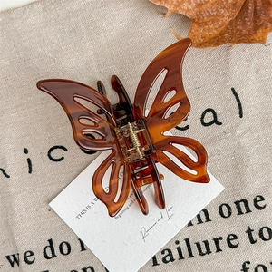 Macro detail of amber butterfly hair claw clip with golden metal spring on fabric