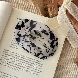 Detailaufnahme einer ovalen Haarklammer mit Marmormuster aus Acetat auf einem Buch
