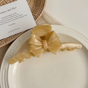 Macro shot of elegant acetate bow hair claw clip in amber marble texture on a white tray