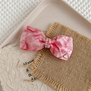 Close-up of pink marble texture bow hair clip with luxury rhinestones and gold VD logo