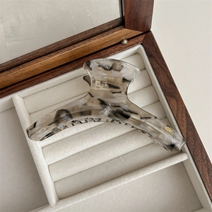 Detail of handmade acetate hair claw with wood grain texture and gold logo in jewelry box