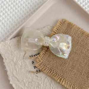 Macro detail of luxury bow hair clip showing pearlescent resin and crystal inlay