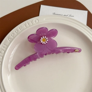 Gros plan d'une grande pince à cheveux fleur violette en acétate sur une assiette blanche