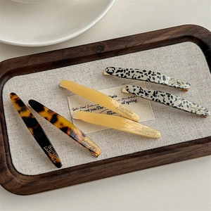 Three acetate hair clips in tortoiseshell and solid colors with gold lettering