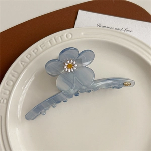 Détail de la grande pince à cheveux bleue en acétate avec marguerite blanche et logo doré
