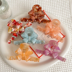 Handmade acetate bow hair claws in six colors displayed on a decorative white tray
