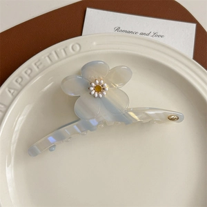 Détail d'une pince à cheveux fleur en acétate bleu clair avec marguerite sur une assiette