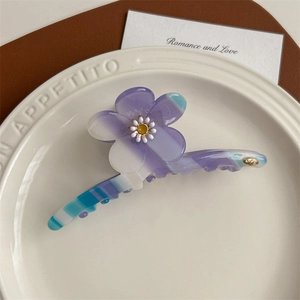 Détail d'une pince à cheveux fleurie en acétate avec logo doré et dégradé élégant