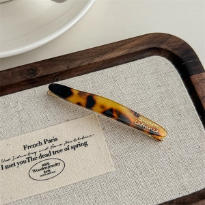 Detail of tortoise shell acetate hair clip with gold lettering on a wooden jewelry tray