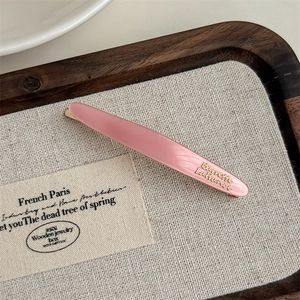 Detail of pink acetate hair clip with golden Barrette La France text on wood tray